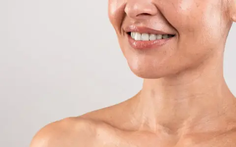 Sorriso radioso con labbra lucide e denti bianchi. La pelle del collo mostra le delicate "collane di Venere", segni di bellezza naturale.