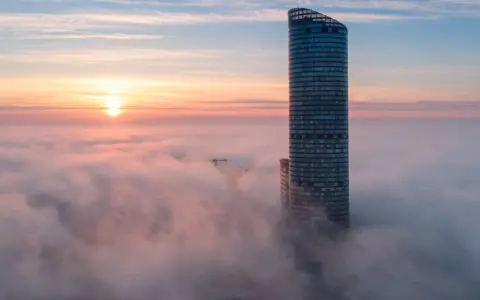 Sky Tower Wrocław, jego imponująca wysokość ginie we mgle o wschodzie słońca. Widok zapiera dech.