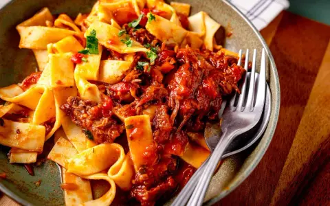 Breite Bandnudeln mit herzhaftem Ragu-Sauce, garniert mit frischer Petersilie. Ein Gabel liegt bereit.