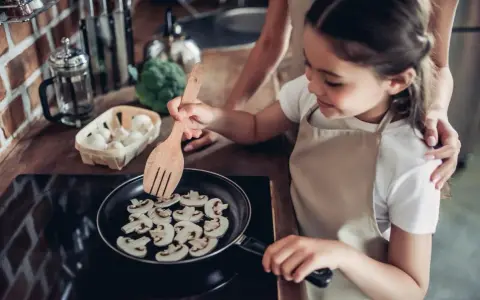Mała kucharka smaży pieczarki na patelni. Czy dzieci mogą jeść pieczarki? Tak, to zdrowy dodatek do posiłków!