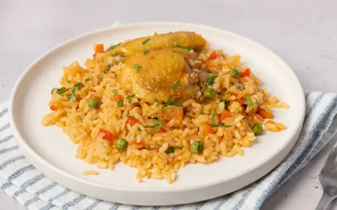 Arroz con pollo jugoso con verduras y perejil picado en un plato blanco.