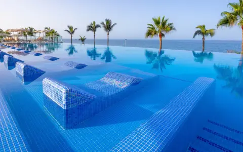 Piscina a sfioro con lettini integrati e palme, vista mare. Un sogno al searesort Riu Gran Canaria.