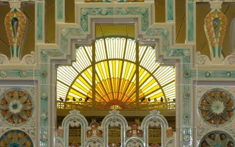Détails ornementaux en céramique, style art déco, encadrant une verrière jaune rayonnante.
