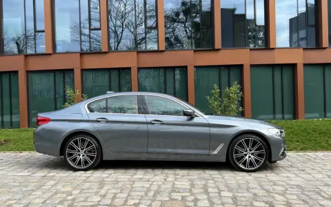 Szary sedan BMW G30 na tle nowoczesnego budynku.