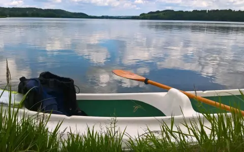 Wiosło i plecak w łodzi na spokojnym jeziorze raduńskim dolnym. Chmury odbijają się w tafli wody.