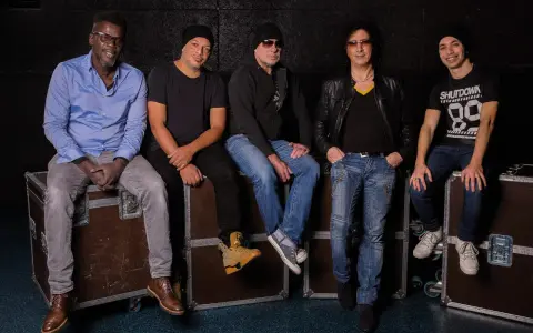 Les membres de Trust (groupe) posent ensemble, assis sur des flight cases, prêts pour leur prochaine performance.
