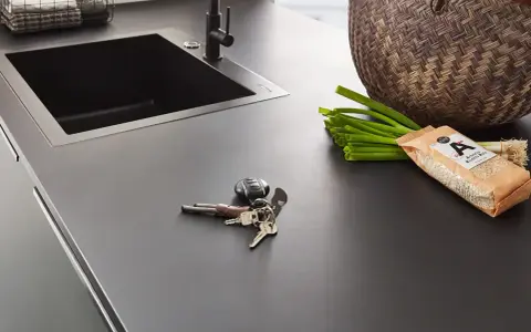 Dunkle Nobilia Arbeitsplatte mit Spüle, Schlüsselbund, Frühlingszwiebeln und Reis. Xtra Arbeitsplatte Nobilia Erfahrung: Praktisch und stilvoll.