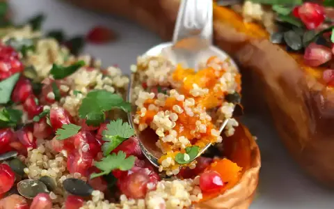 En sked tar en portion av ett läckert quinoa recept fyllt med pumpa, granatäpple och örter, serverat i en ugnsbakad butternut squash.