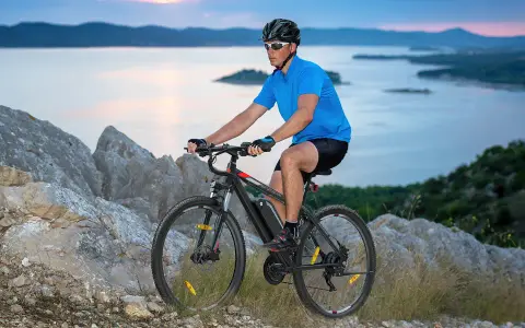 Man riding a mountain bike on a rocky trail overlooking a serene bay at dusk.