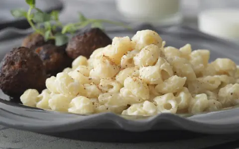 En tallrik med stuvade makaroner och köttbullar, garnerat med en kvist örter. En klassisk svensk rätt som värmer själen.