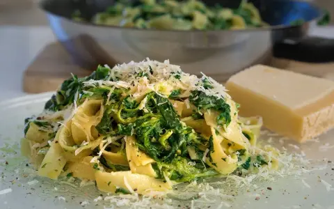 Makaron tagliatelle ze szpinakiem i startym parmezanem, obok kawałek sera.
