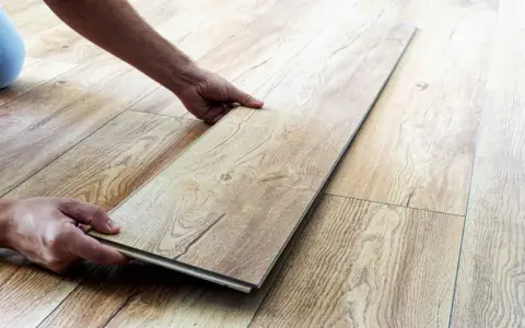 Man's hands placing a laminate plank to repair suelo laminado.
