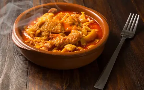 Un plat fumant de tête de veau mijotée, rappelant la recette tête de veau grand mère, servi dans un bol en terre cuite avec une fourchette.