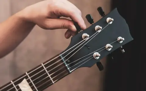 Dłoń kręci kluczem, strojąc gitarę. Słychać czysty dźwięk e, gotowy do gry.