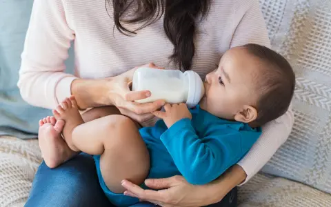 Mama karmi dziecko butelką. To przykład karmienia mieszanego, gdzie dziecko otrzymuje zarówno mleko matki, jak i mleko modyfikowane.