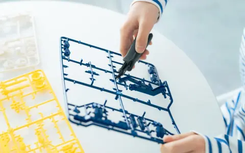 Dłoń trzymająca cążki odcina niebieskie elementy z ramki modelu.