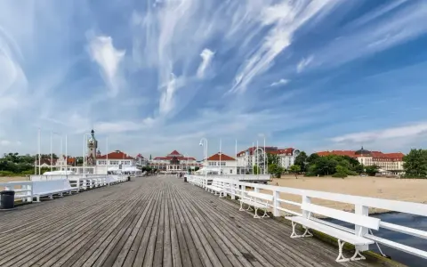 Drewniane molo w Sopocie, z widokiem na plażę i zabytkowe budynki. To popularne sopockie atrakcje, idealne na spacer.