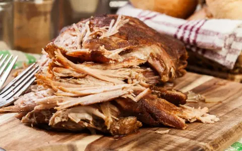 Szarpana łopatka wieprzowa na desce, obok widelce i ręcznik.
