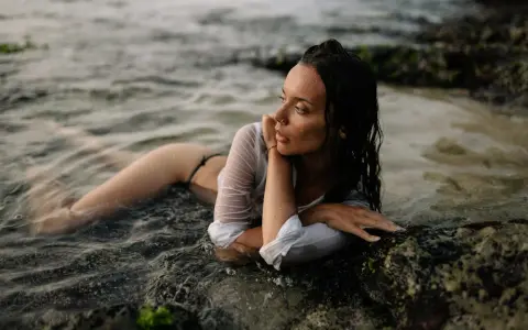 Modella in posa foto artistiche da fare al mare, sdraiata tra le rocce e l'acqua.