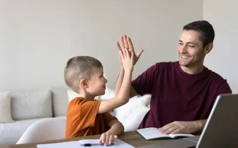 Ojciec i syn dają sobie piątkę, świętując sukcesy w nauce. To chwila radości, kiedy nie stawiamy przecinka, bo wszystko jest jasne.