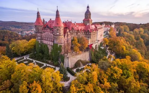 Zamek Książ otoczony jesiennym lasem, z widoczną palmiarnią w oddali.