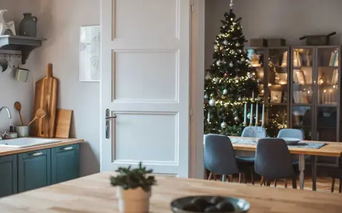 Julstämning i köket med en öppen dörr som avslöjar ett vackert julpyntat träd och en matsal. Perfekt jul inredning inspiration.