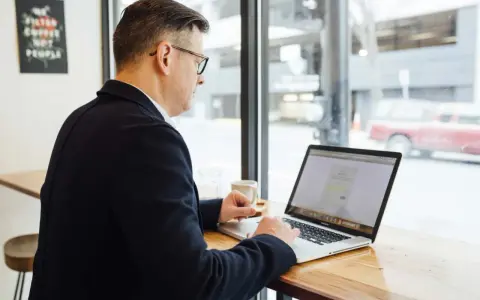 Hombre revisa en su laptop una cotización a tiempo parcial a efectos de jubilación, sentado en una cafetería.