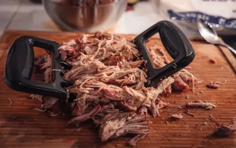 Pulled pork mit Fleischgabel auf Holzbrett. Perfekt für Smoker Rezepte Schwein, z.B. Pulled Pork Sandwiches.