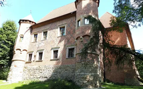 Zamek w Dębnie Polskim, ceglana budowla z kamiennym cokołem, otoczona zielenią.