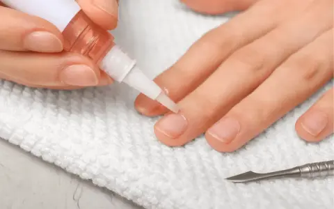 Application d'huile sur les cuticules des ongles pour un soin hydratant. Un petit pinceau dépose le produit sur le contour de l'ongle.