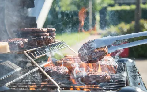 Des hamburgers grillent sur un barbecue à gaz. La cuisson est intense, la fumée s'élève. Nettoyer barbecue gaz après ce festin sera nécessaire.