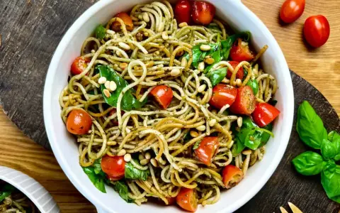 Leckerer Spaghetti-Salat zum Grillen mit Kirschtomaten, Pinienkernen und frischem Basilikum in einer weißen Schüssel.