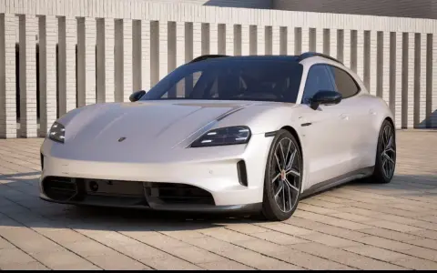 Elegancki Porsche Taycan w kolorze jasnoszarym, zaparkowany przed nowoczesnym budynkiem. Sprawdź porsche taycan cena!
