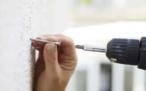 Mano insertando un tornillo en una pared texturizada, útil para saber si una pared es de pladur.