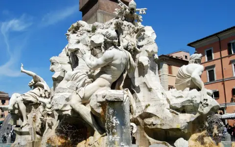Fontana dei Quattro Fiumi di Bernini in Piazza Navona, Roma. Sculture maestose e acqua zampillante sotto un cielo azzurro.
