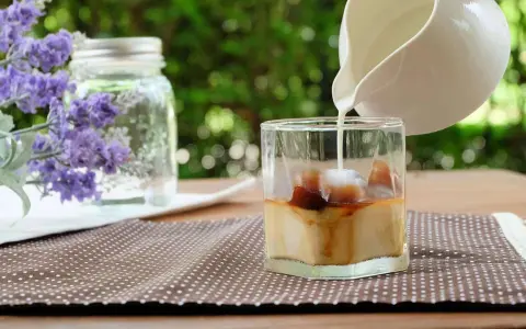 Milch wird in ein Glas mit Eiswürfeln und Kaffee gegossen, um einen erfrischenden Lavendel Latte zuzubereiten.