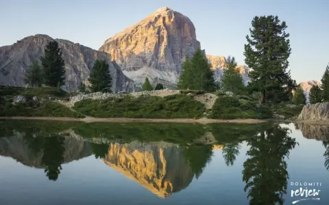 Riflesso perfetto di una montagna imponente nel lago di Limides, con alberi verdi e cielo azzurro.