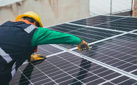 Handwerker mit gelbem Helm montiert Solarmodule für solarstrom einspeisen.