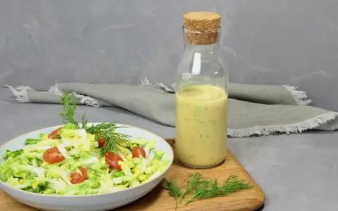 Frischer Salat mit Tomaten und Mais, daneben eine Flasche mit cremigem Jogurt Dressing und Dill.