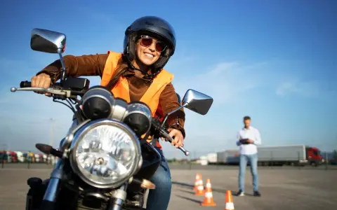 Uśmiechnięta kursantka na motorze, w kamizelce odblaskowej i kasku, uczy się jeździć. Zastanawiasz się, ile kosztują prawo jazdy na motor?