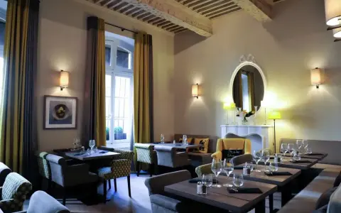Salle à manger élégante avec tables dressées, prête à servir une spécialité de Provence. Lumière douce, rideaux ocre et gris, miroir orné.