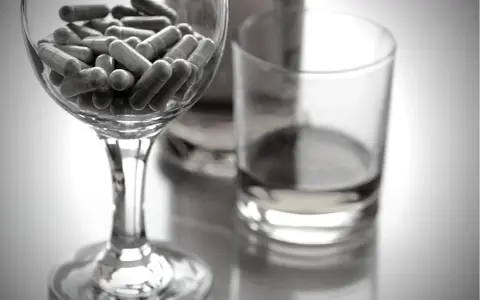 Kapsułki w kieliszku, obok szklanki z płynem. Czy niektóre leki zawierają alkohol etylowy?