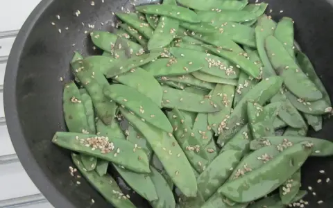 Pois gourmand croquants saupoudrés de graines de sésame dans une poêle.