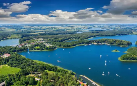 Malownicze, klimatyczne miejsca nad jeziorem, gdzie lasy schodzą do wody, a żaglówki unoszą się na błękitnej tafli.