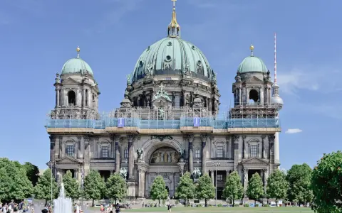 Berlins domkyrka med sina imponerande kupoler är ett måste när man undrar vad ska man se i Berlin. En fontän och grönskande träd ramar in den vackra byggnaden.