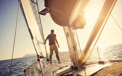 Mann auf einem Segelboot, das die Sonne genießt. Verschiedene kleine Segelboote Typen sind auf dem Meer unterwegs.
