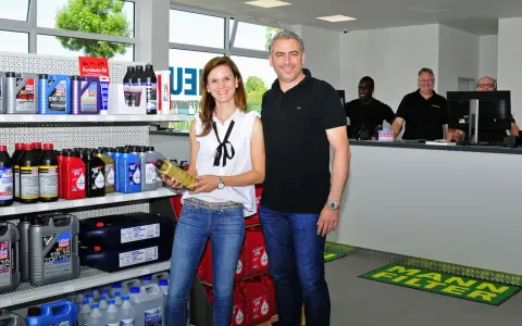 Ein Mann und eine Frau stehen vor Regalen mit Autoteilen und Ölflaschen.