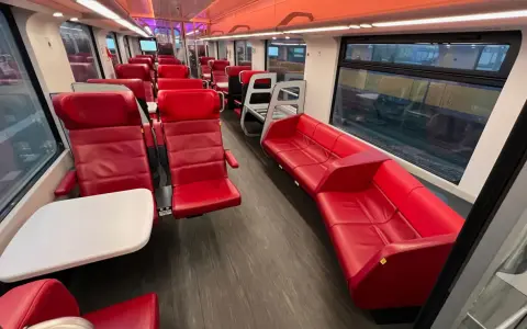 Interior of a modern train, with red leather seats and tables, ready for a journey from AMS to Brussels.