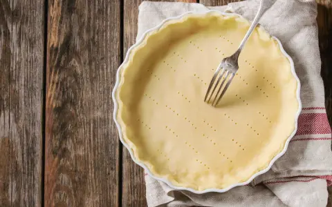 Pâte brisée sans beurre dans un plat à tarte, prête à être garnie. Une fourchette est plantée dans la pâte.