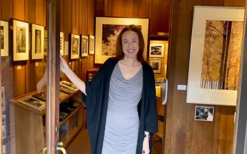 A woman smiles, opening the door to a photography west gallery filled with framed prints and display cases of artwork.